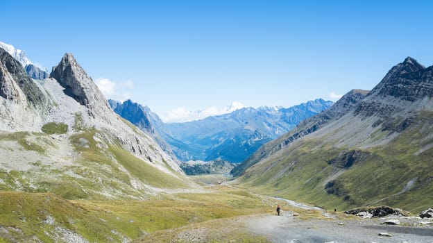 SEIGNE HILL, ITALY - AUGUST 27: Hikers on hill path with snowy Grand Combin mountain in the background. The region is a stage of the popular Mont Blanc tour. August 27, 2014 in Seigne Hill.