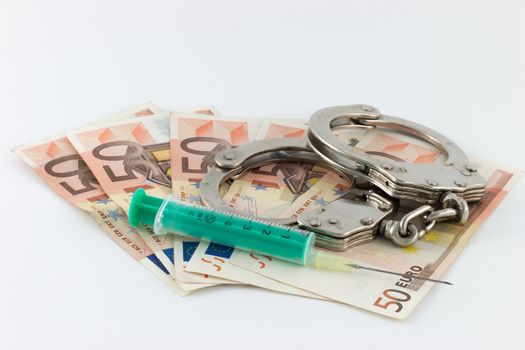 Handcuffs with signs of use and syringe with green flask on bills