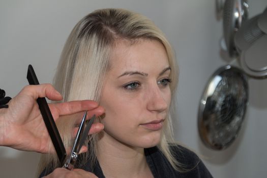 Beautiful blond girl getting a haircut in a hairdresser's shop
