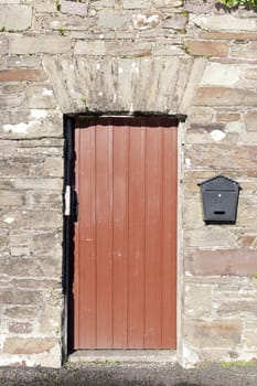 brown wooden doorway and a post box on old stone wall