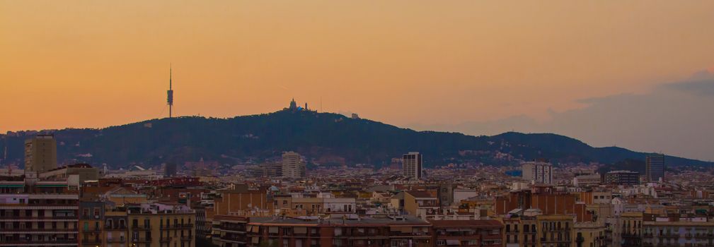 Panorama of Barcelona skyline, with buildings in the foreground and mountains in the background, at sunset