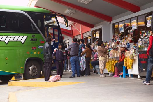 BANOS, ECUADOR - FEBRUARY 22, 2014: Unidentified people at the bus terminal with a bus standing in the back and snack stands on the side on February 22, 2014 in Banos, Ecuador. 