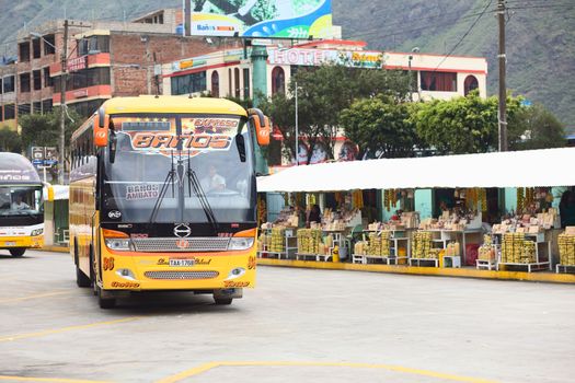 BANOS, ECUADOR - FEBRUARY 22, 2014: Bus of the Expreso Banos transportation company in the bus terminal with a row of small stands offering sweets and sugar cane in the back on February 22, 2014 in Banos, Ecuador. 