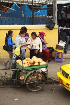 AMBATO, ECUADOR - MAY 12, 2014: Unidentified people on the sidewalk with a small cart of coconuts on the roadside on May 12, 2014 in Ambato, Ecuador.