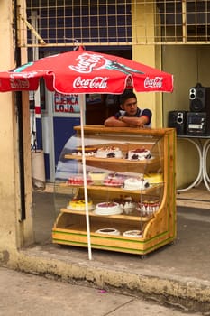 AMBATO, ECUADOR - MAY 12, 2014: Unidentified young an standing at a glass case with many different cakes on May 12, 2014 in Ambato, Ecuador.