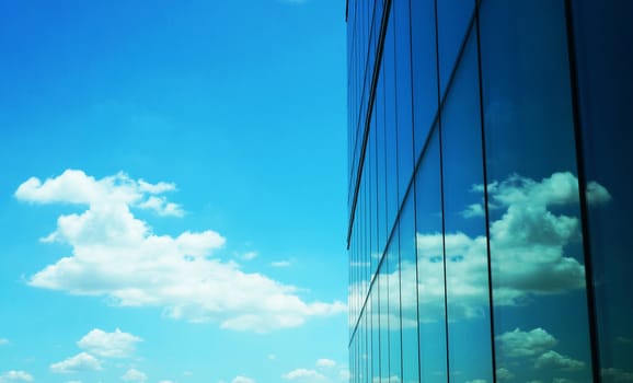 Skyscraper with modern style creating a mirror and reflecting  of beautiful clouds  on blue sky.                               