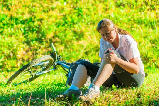 cyclist holds a his bruised knee while sitting on the lawn