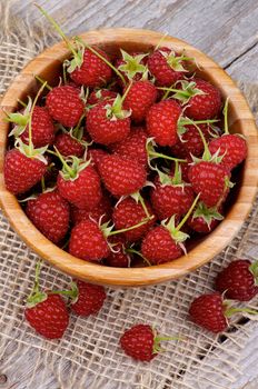 Perfect Ripe Raspberries with Stems in Wooden Bowl on Sackcloth and Wooden background. Top View