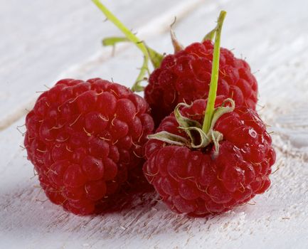 Three Perfect Ripe Forest Raspberries with Stems and Droplets isolated on White Wooden background