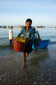 PHAN THIET- VIETNAM- JAN 21:  Seafood market on beach, people trader fishing product in morning, boat on water,  person carry fresh food, Viet Nam, Jan 21, 2014