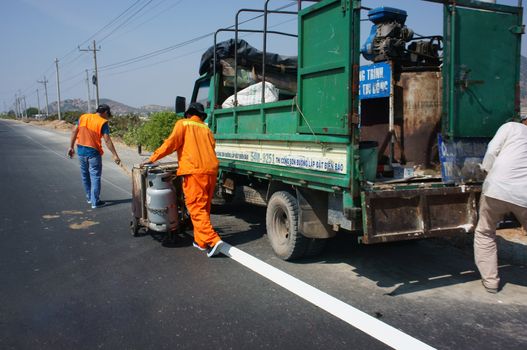 BINH THUAN, VIETNAM- JAN 23: Team of civil worker work on highway, they draw white line on road with eject machine, truck transport public work tool to traffic project , Viet Nam, Feb 23, 2014