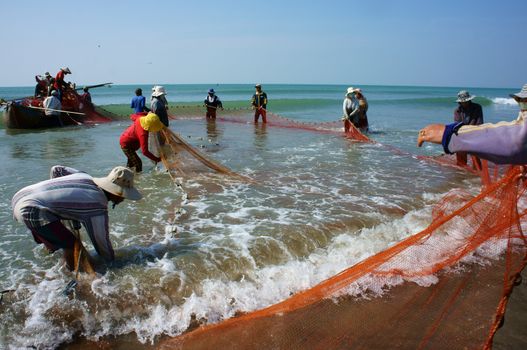 BINH THUAN, VIETNAM- JAN 22: Team work of fisherman on beach, group of people pull fishing net to catch fish, stand in row, person move to seashore, crowded atmosphere, fresh air,Viet Nam, Jan22, 2014