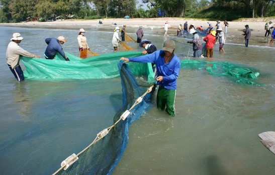 BINH THUAN, VIETNAM- JAN 22: Team work of fisherman on beach, group of people pull fishing net to catch fish, stand in row, person move to seashore, crowded atmosphere, fresh air,Viet Nam, Jan22, 2014