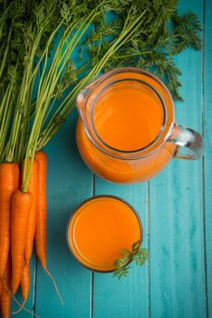 Homemade natural carrot juice in glass on rustic blue wooden table in background