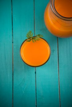 Homemade natural carrot juice in glass on rustic blue wooden table in background