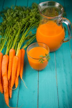 Homemade natural carrot juice in glass on rustic blue wooden table in background