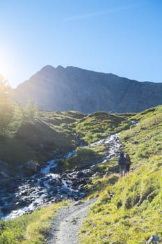 COMBAL, ITALY - AUGUST 28: Hikers walking up path by creek with Charmonts Peaks in the background. The area is on a stage of the popular European Mont Blanc tour. August 28, 2014 in Combal.