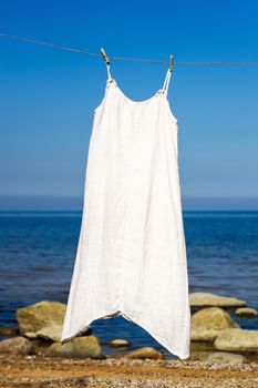 White dress hanging on a rope on the sea background