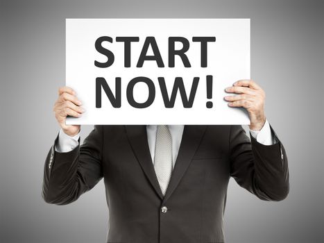 A business man holding a paper in front of his face with the text start now