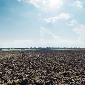 sun in clouds over black field after harvesting