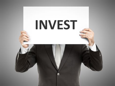 A business man holding a paper in front of his face with the word invest