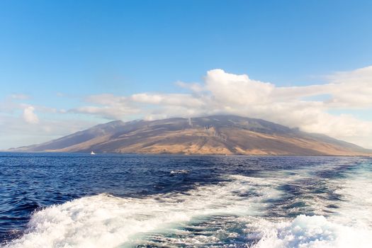The island of Maui seen from the ocean over the wake of a motorboat