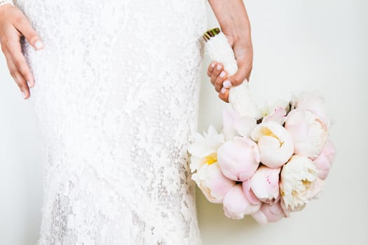 Woman Holding a nice Wedding Bouquet in front of a white Wall