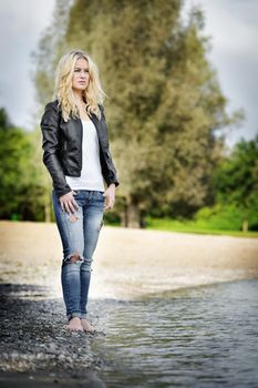 Blond young woman standing barefoot on the edge of a lake