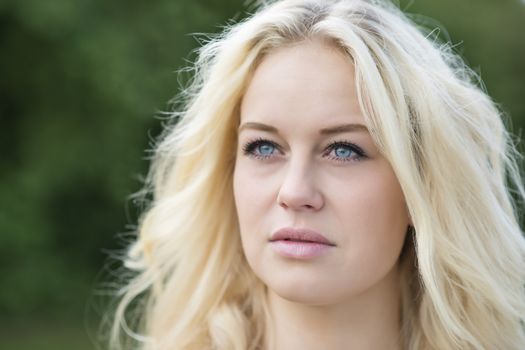 Outdoor portrait of a young blond woman in summer with green background