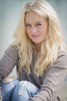 Blond woman sitting at the edge of a lake in summer