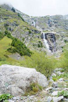Natural cascade on hillside in La Fouly, Switzerland, and white bolder in the foreground.