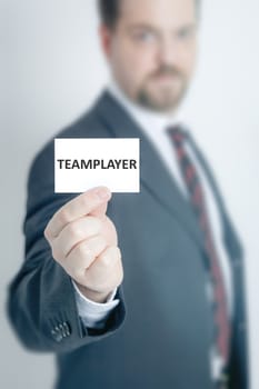 A business man holding a card with the word teamplayer