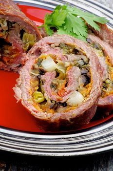 Slices of Rolled Beef Meatloaf Stuffed with Leek, Carrot and Greens closeup on Red Plate