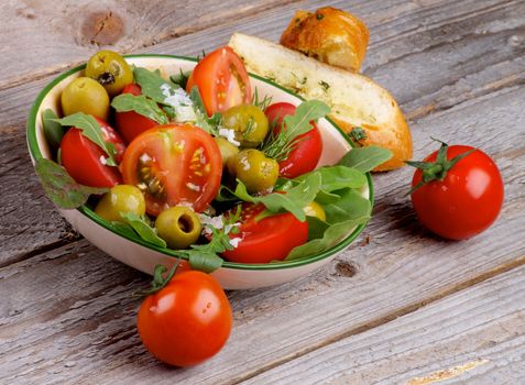 Fresh Tomatoes Salad with Arugula, Olives, Greens, Garlic Bread and Cherry Tomato Full Body isolated on Rustic Wooden background