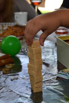 child's hand doing a sugar tower on a table