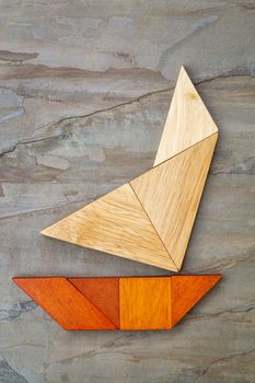 abstract picture of a sailing yacht built from seven tangram wooden pieces over a slate rock background, artwork created by the photographer