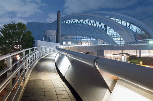 pedestrian pathway with metallic handrail leads toward modern arc dome building by night
