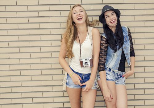 Two beautiful and young girlfriends having fun, in front of a brick wall