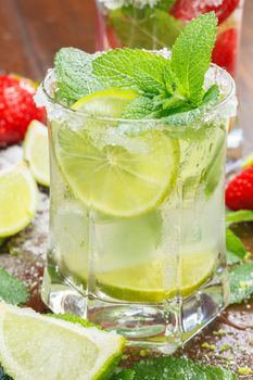 Glass of cocktails with ice, mint, strawberry and lime on wooden table