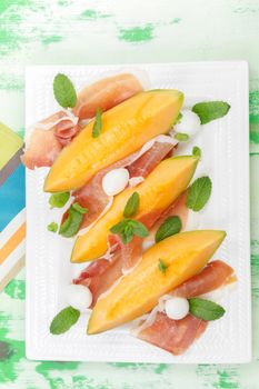 Sliced prosciutto and melon on plate over old rustic wooden background