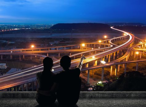 Silhouette of couple sit on ground point faraway on the roof above the city in the night.