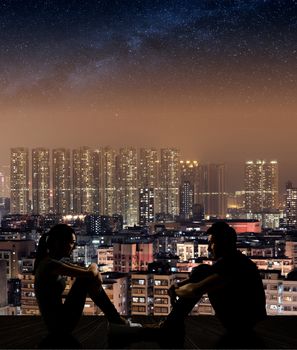 Silhouette of young couple face to face sit on ground in the city night.