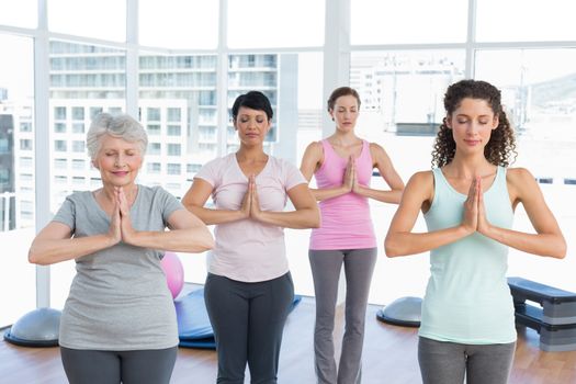 Female trainer with class standing in namaste pose at yoga class