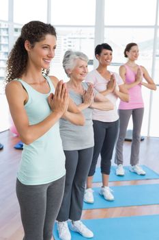 Happy female trainer with class standing in namaste pose at yoga class