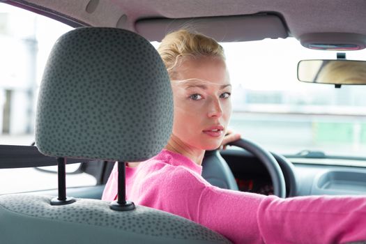 Beautiful young lady looking back through the rear window from the front seat of a car while reversing.