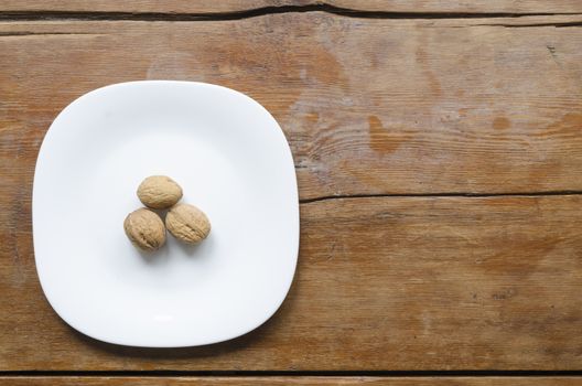 white ceramic dish with three walnuts on the vintage wooden table