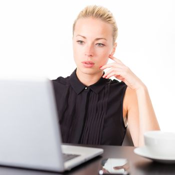 Business woman checking some information on her laptop computer in office. White cup of coffee on the desk. 