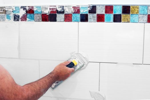 Man grouting wall ceramic tiles with float