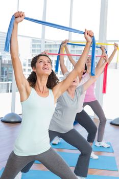 Happy female trainer with class holding up exercise belts at yoga class