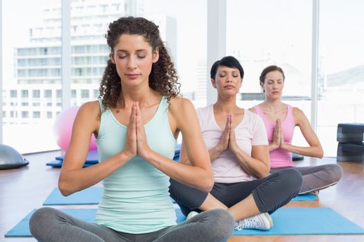 Sporty young women with eyes closed and joined hands at a bright fitness studio